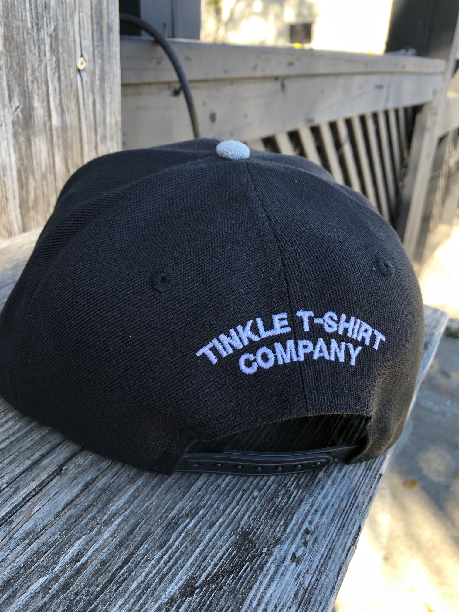back of Black and grey flat bill snapback hat with embroidered Inlet Tinkler logo on the front Tinkle T shirt company on the back photo at marshwalk