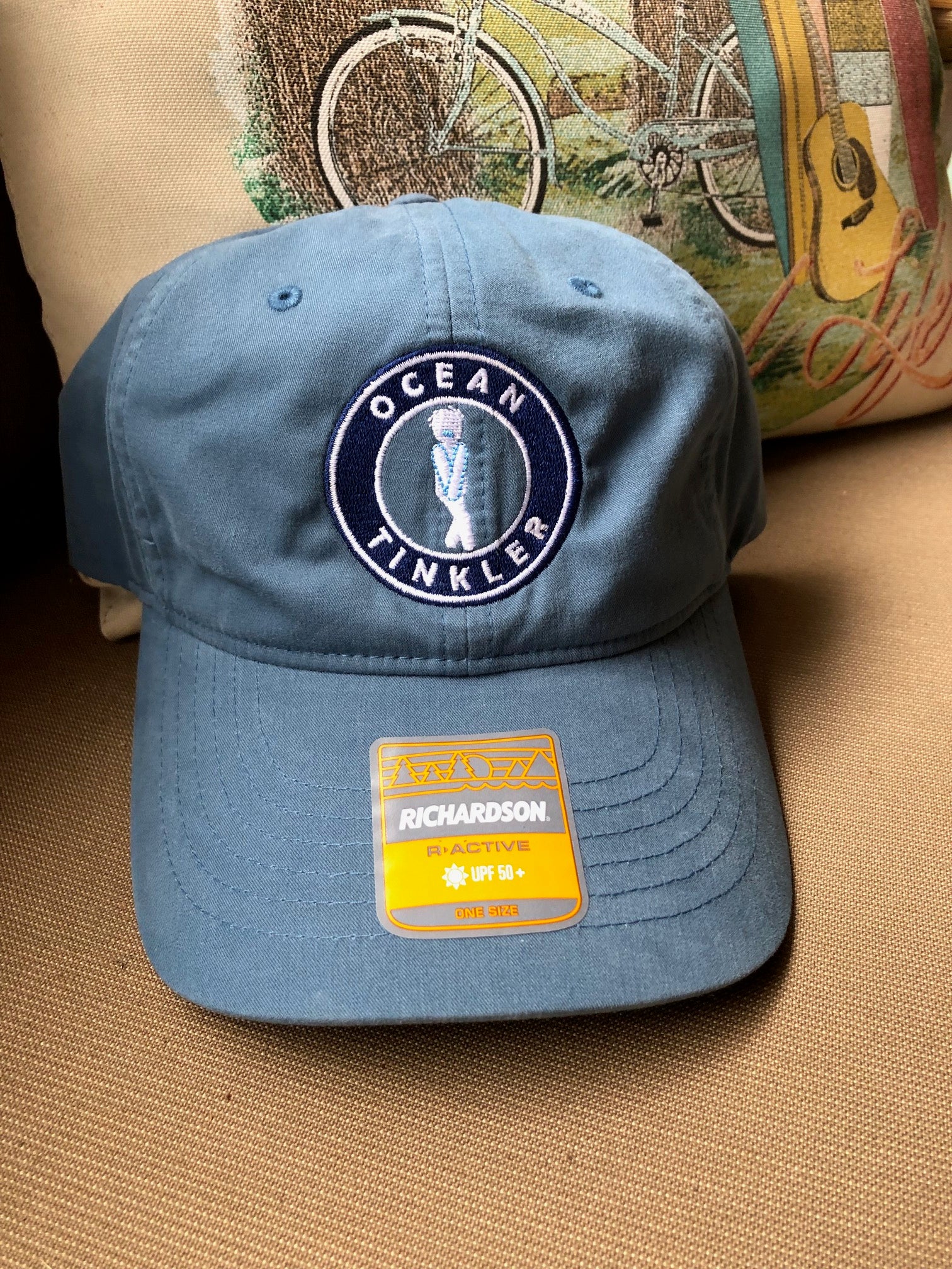 Front view of light blue Ocean Tinkler performance hat with embroidered logo richardson uv protection sticker